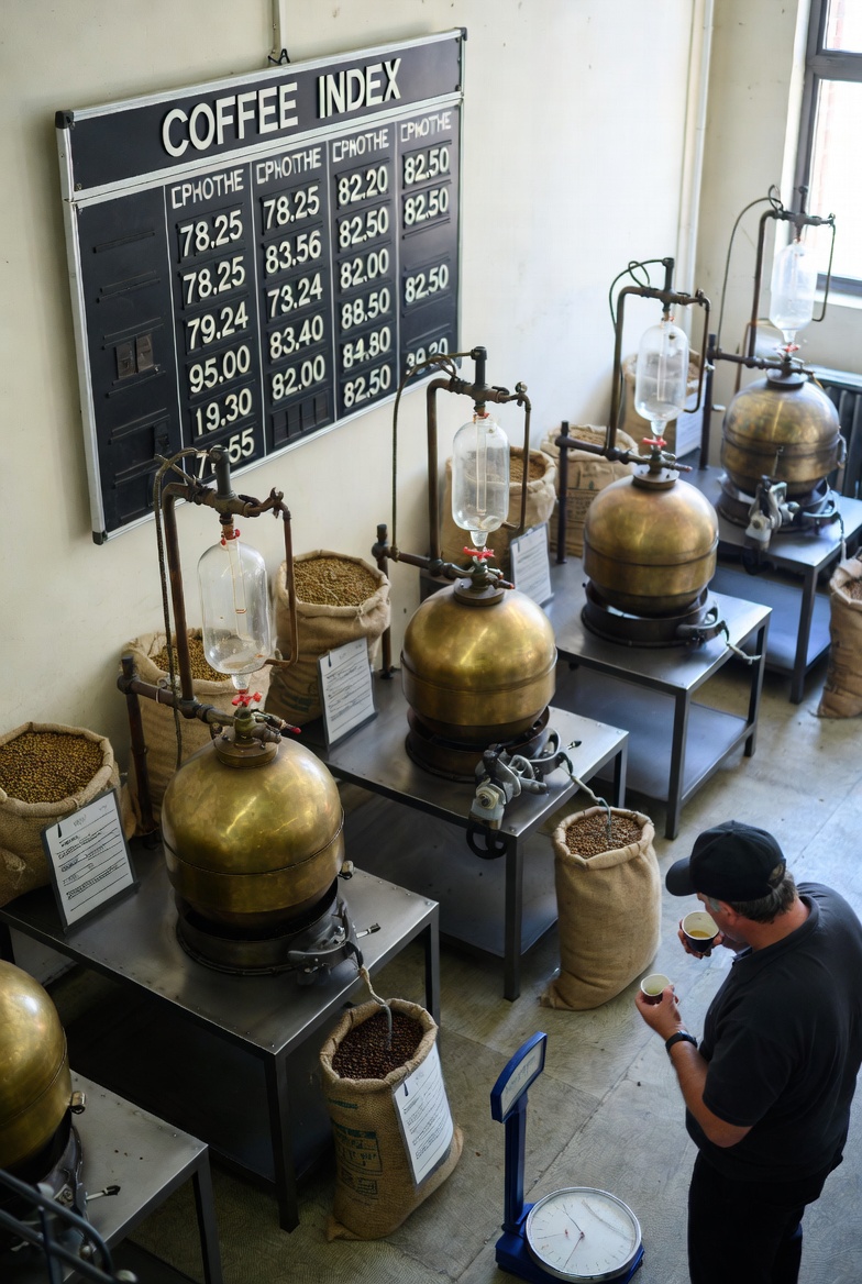 Brass coffee roasters and bean sacks under a coffee index board