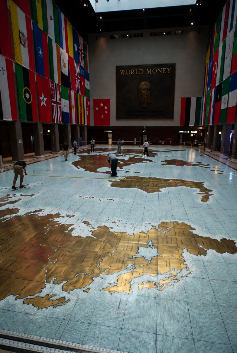 A hall with a giant brass world map on the floor and national flags above